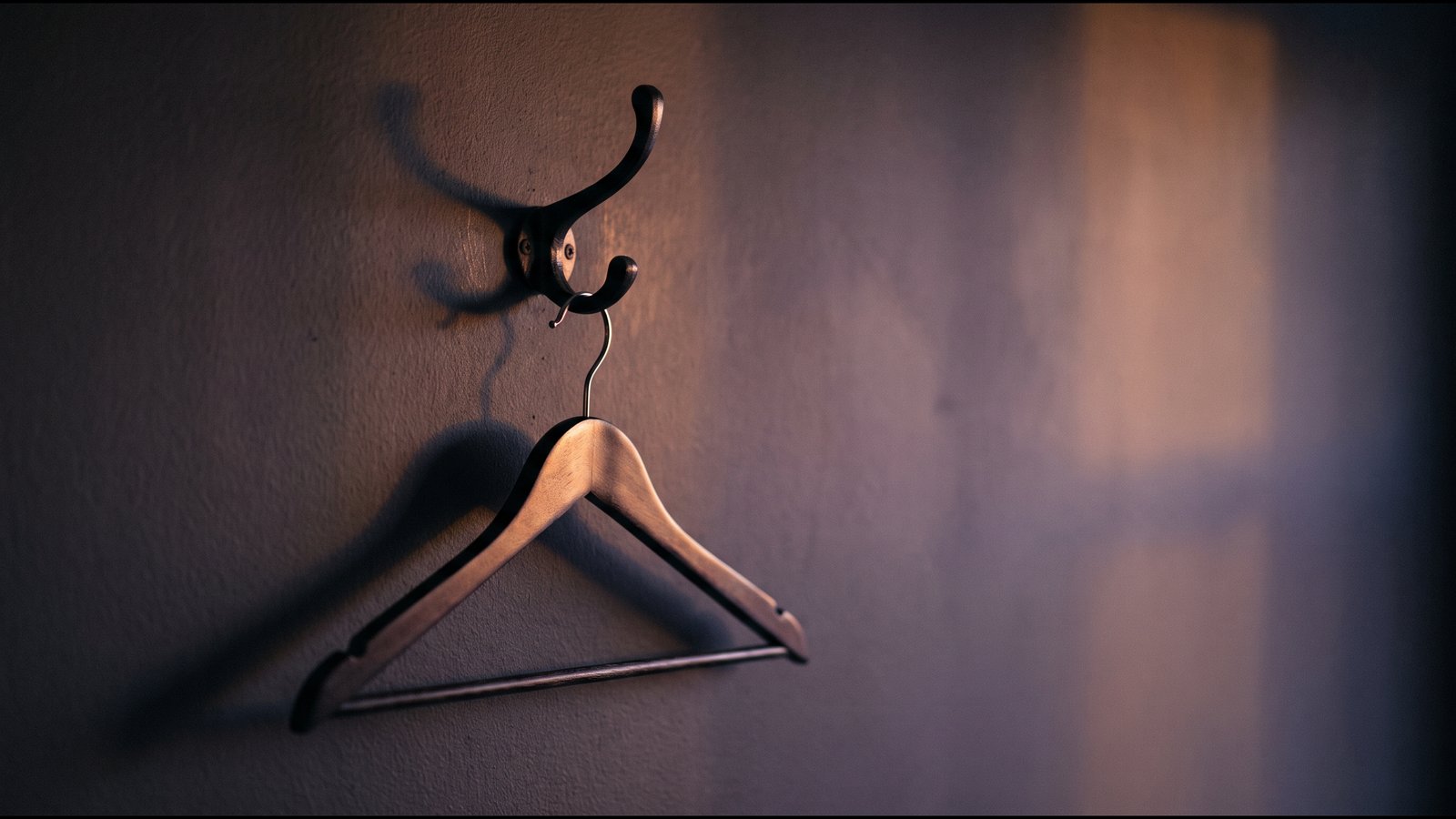 A coat hook on a dark wall with a single empty hanger